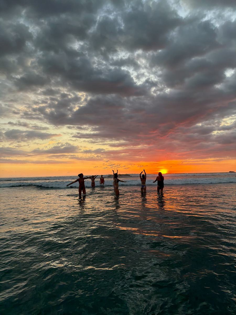 Women standing in the shallows at Playa Guiones as the sun drops into the Pacific