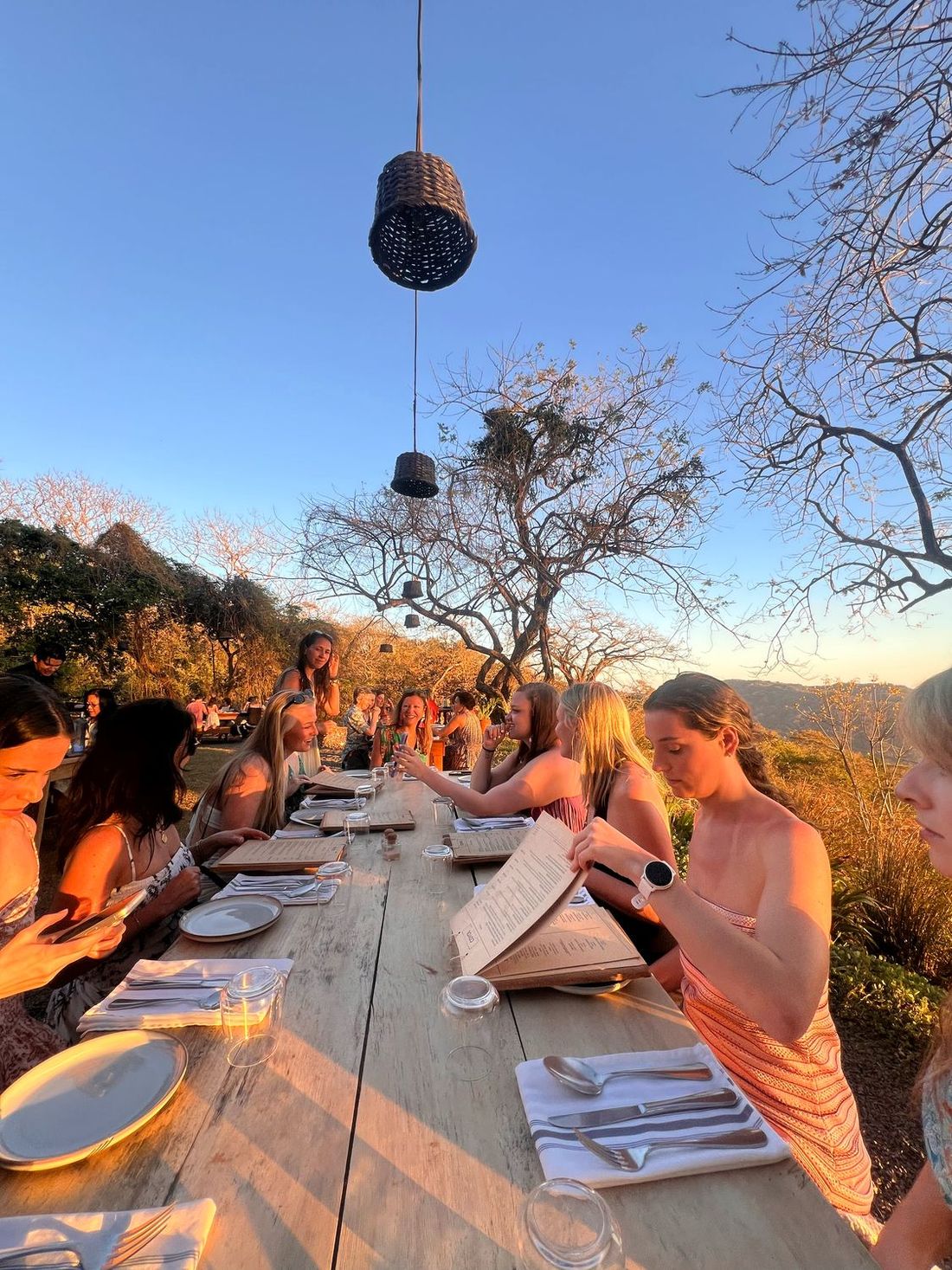 A long table set for dinner outdoors as the sky turns orange