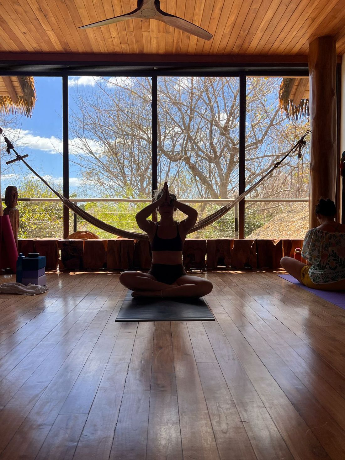 A woman seated in meditation on the villa’s open-air yoga deck, jungle framed in the windows behind her